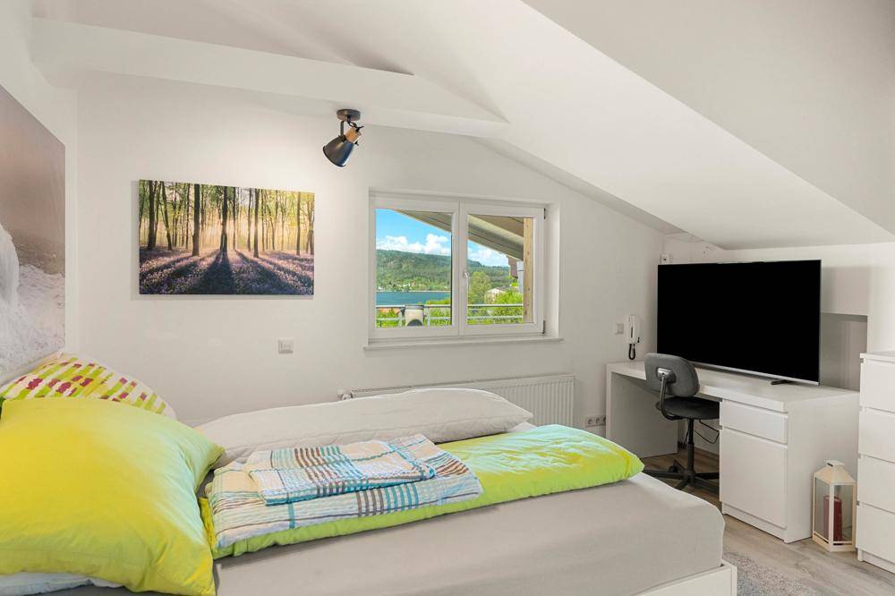 Schlafzimmer im Dachgeschoss mit schrägen Wänden, Seeblick und einem Arbeitsbereich.