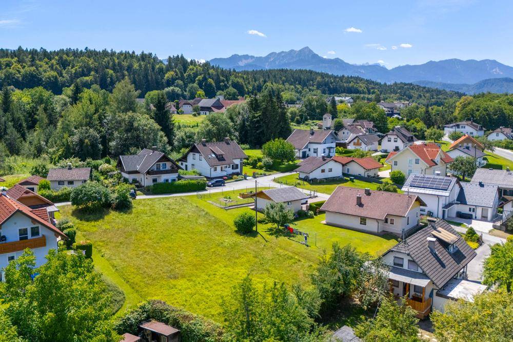 Blick über eine ruhige Wohnsiedlung mit grünen Wiesen und Bergen im Hintergrund.