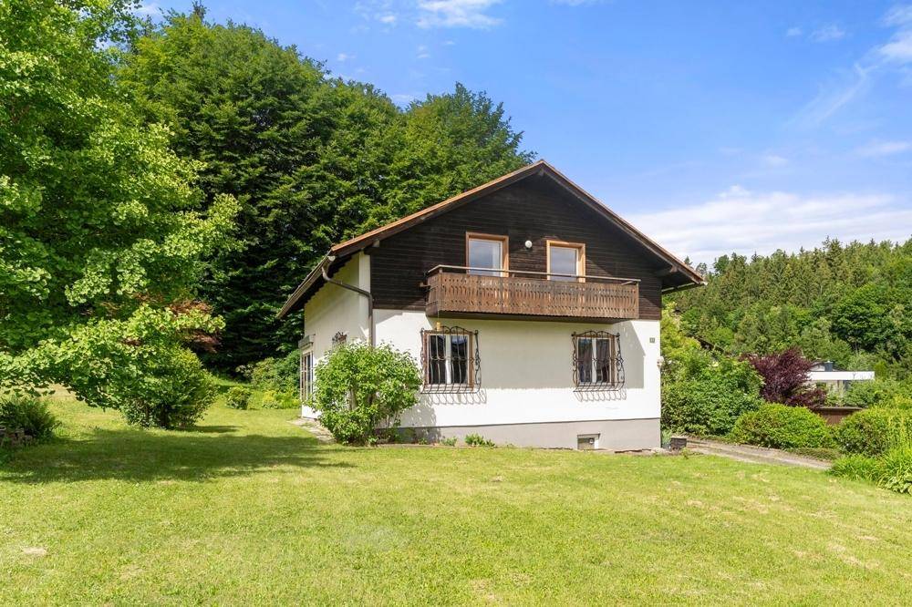 Freistehendes Haus mit Balkon und Satteldach, umgeben von viel Grün.