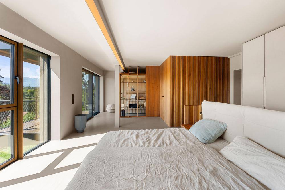 Helles Schlafzimmer mit Holzwandverkleidung und großem Fenster, das Zugang zu einem Außenbereich bietet.