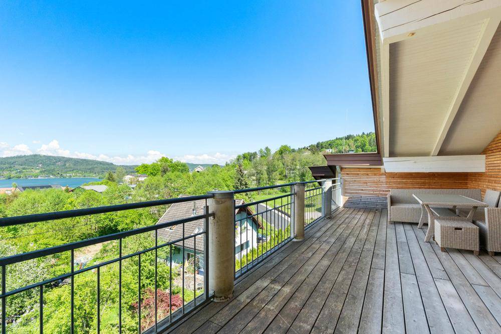 Großer Holzbalkon mit Metallgeländer und weitem Blick auf den See und die grüne Umgebung.