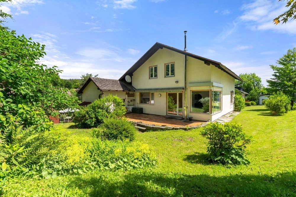 Rückseite des Hauses mit Terrasse und weitläufigem Gartenbereich, umgeben von Bäumen.