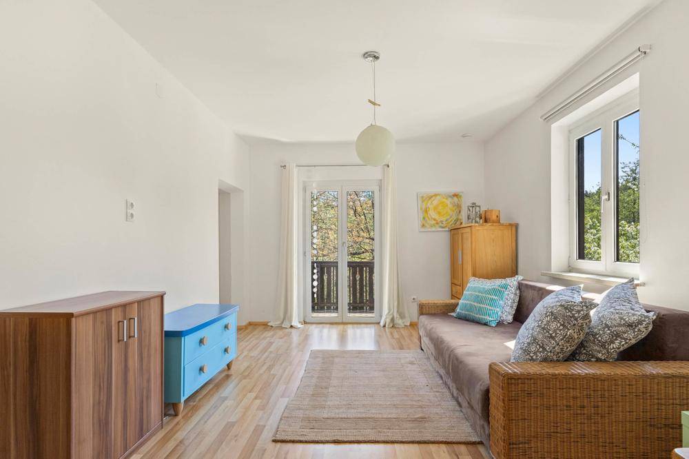 Helles Wohnzimmer mit Sofa, Holzmöbeln und Zugang zu einem Balkon mit Blick ins Grüne.