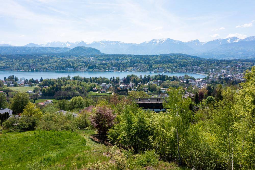 Weitläufiger Ausblick über einen See, bewaldete Ufer und eine Bergkette am Horizont.