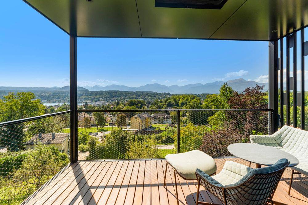 Geräumiger Balkon mit Holzdeck und modernen Möbeln, der einen atemberaubenden Blick auf See und Berge bietet.