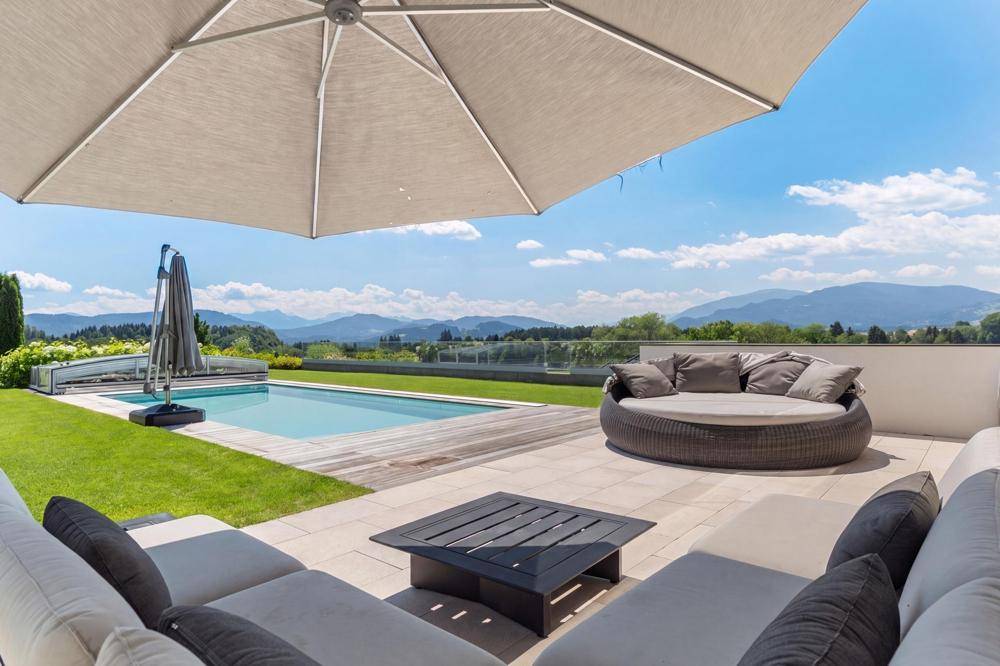 Geräumige Terrasse mit Lounge-Möbeln und Sonnenschirm, bietet einen herrlichen Blick auf den Pool und die Berge.