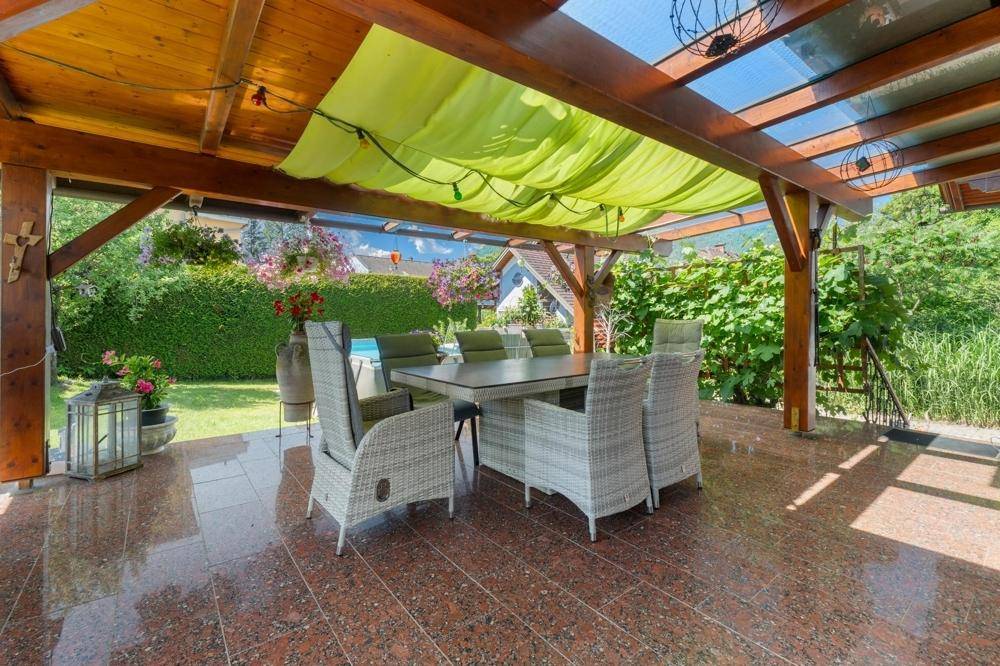 Überdachte Terrasse mit großem Esstisch und bequemen Gartenmöbeln, umgeben von Grün.
