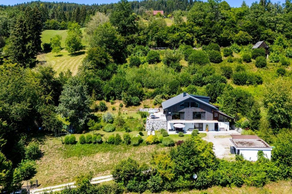 Luftaufnahme des modernen Hauses eingebettet in eine grüne Hügellandschaft mit viel Natur.