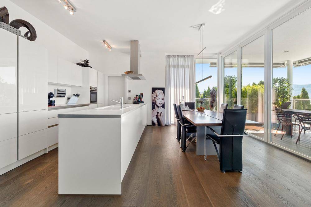 Moderne weiße Küche mit Kochinsel und integriertem Essbereich, hell und mit Zugang zur Terrasse.