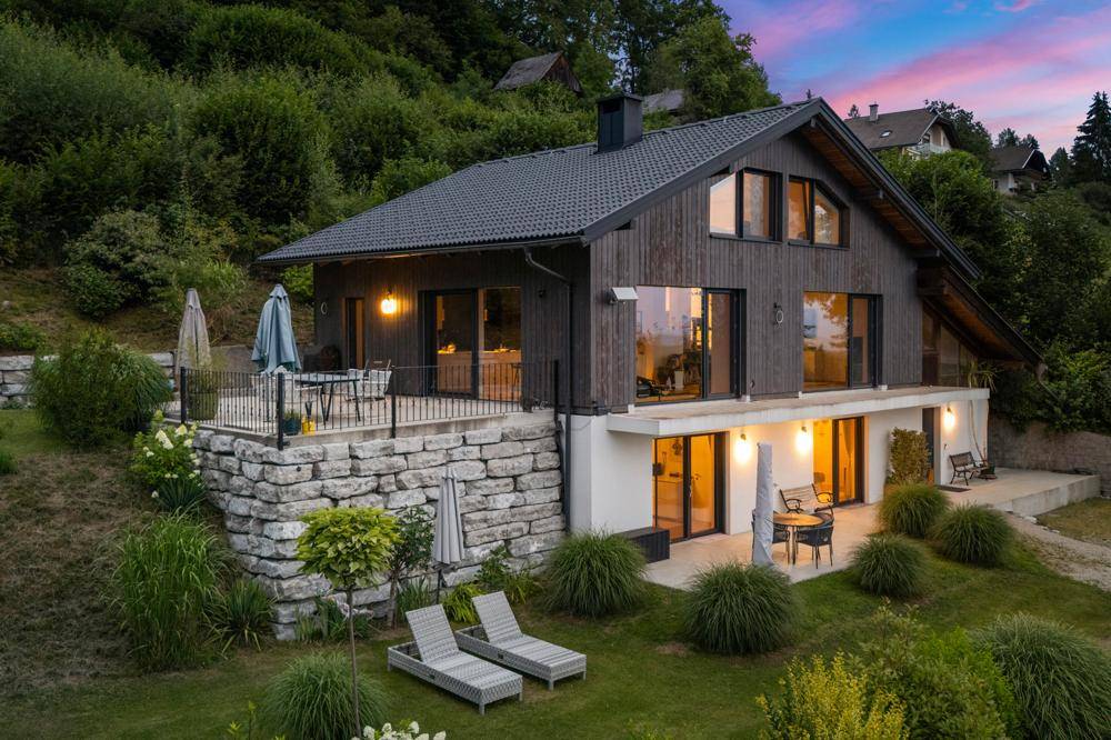 Modernes Haus bei Sonnenuntergang mit beleuchteten Terrassen und Gartenbereichen.