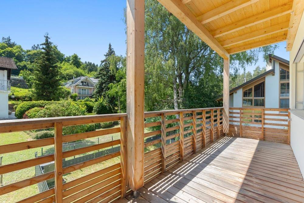 Geräumiger Holzbalkon mit Blick auf die grüne Umgebung und weitere Häuser.