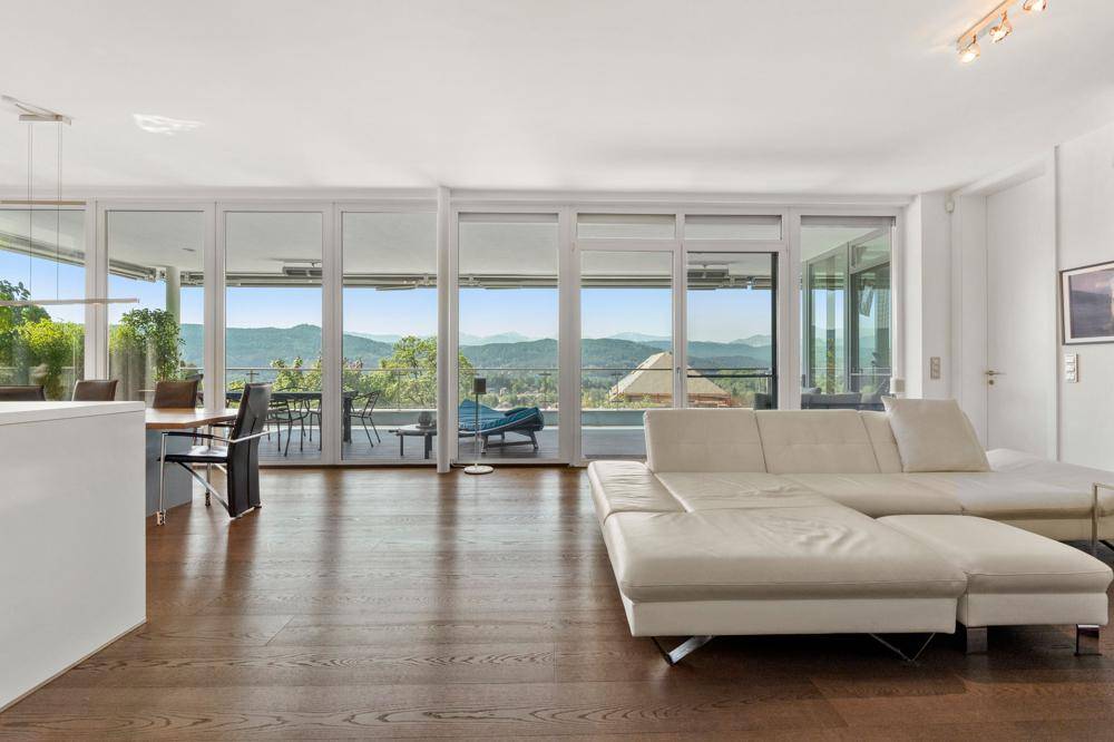 Helles Wohnzimmer mit weißem Sofa, dunklem Parkettboden und raumhohen Fenstern mit Bergblick.