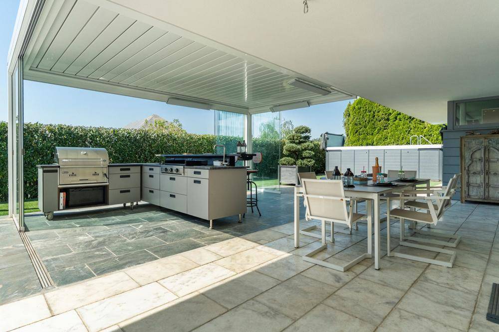 Überdachte Terrasse mit voll ausgestatteter Außenküche, Essbereich und Blick auf den Garten.