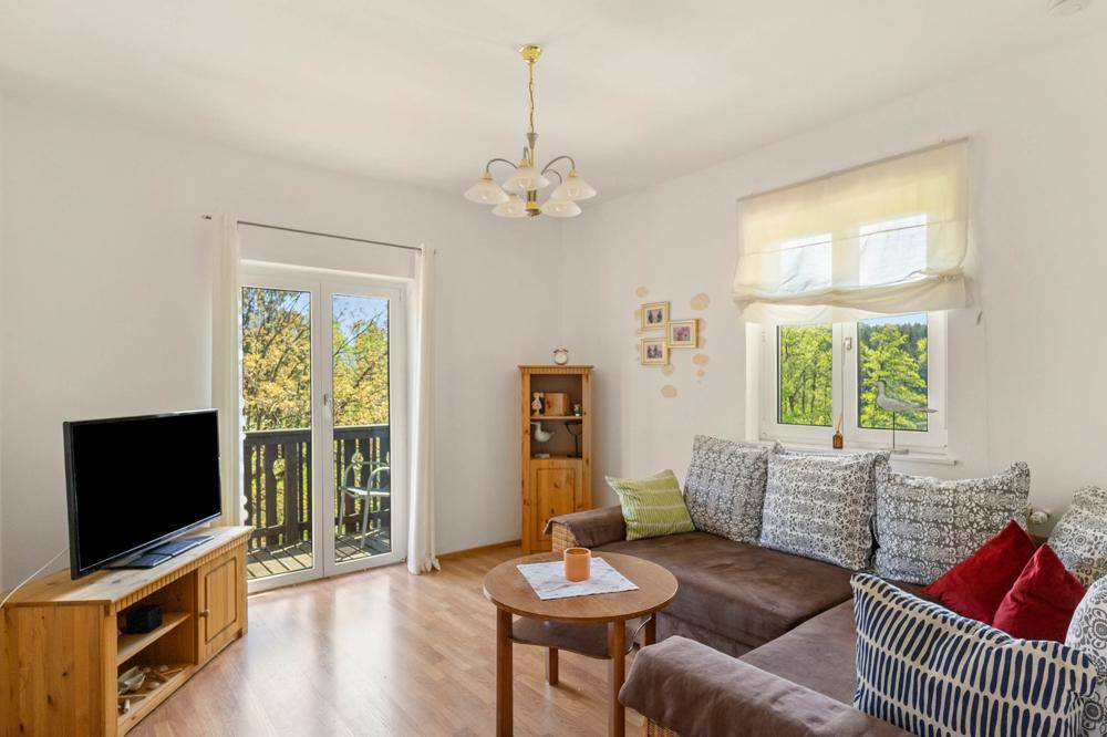 Geräumiges Wohnzimmer mit großem Ecksofa, Fernseher und Fenstern mit Blick auf die Natur.