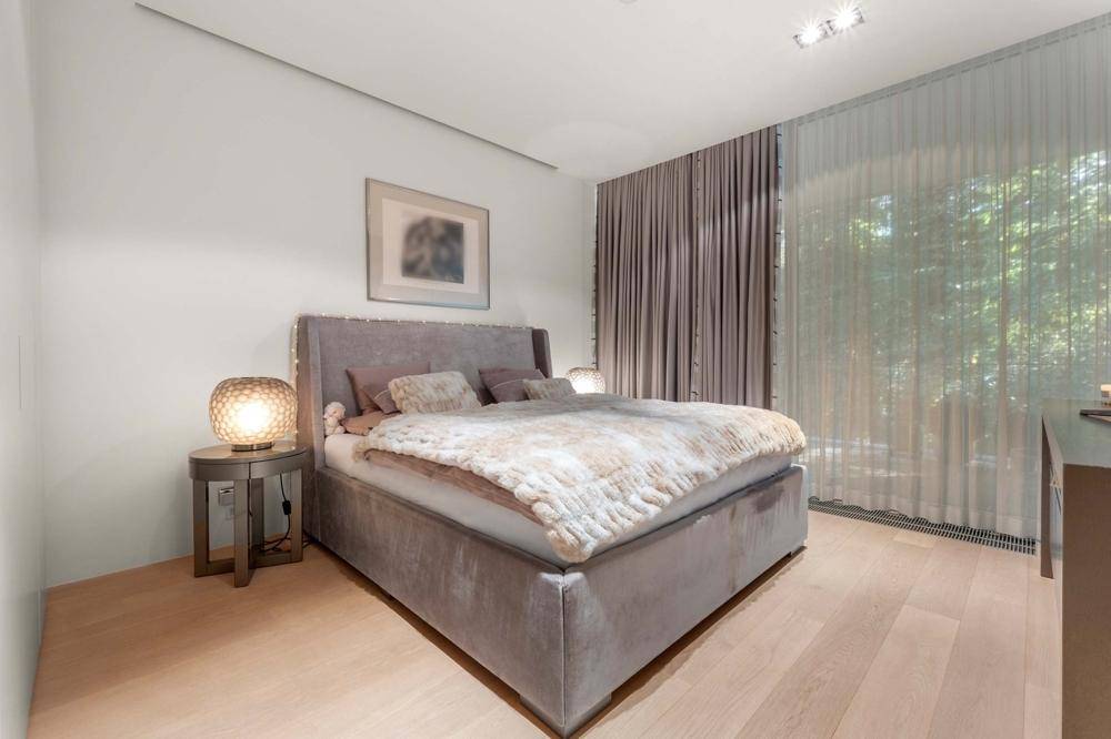 Gemütliches Schlafzimmer mit großem Bett, Holzboden und bodentiefen Fenstern mit Blick ins Grüne.