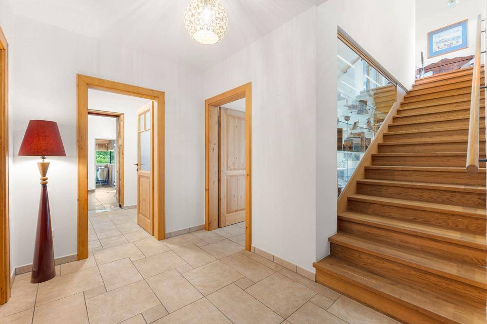 Heller Flur mit Holztreppe, Glasgeländer und Fliesenboden.