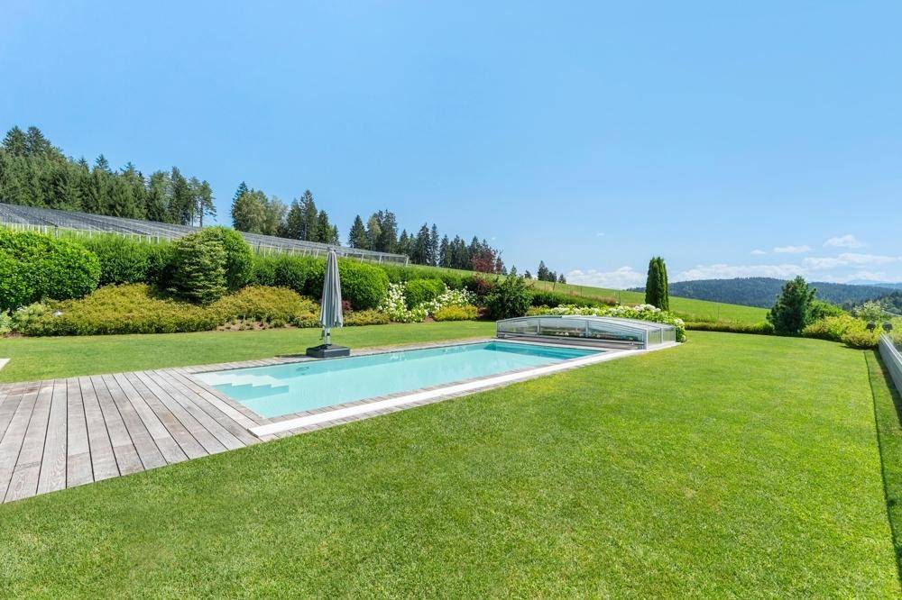 Langer Poolbereich mit Holzdeck, umgeben von einem weitläufigen, grünen Garten und Hügellandschaft.