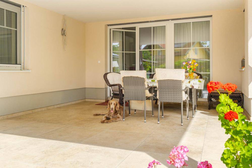 Sonnige, überdachte Terrasse mit Esstisch und Fliesenboden, ideal für entspannte Stunden im Freien.