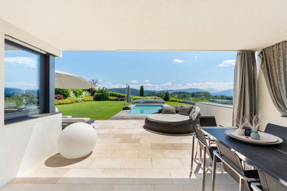 Überdachte Loggia mit Essbereich und Lounge-Möbeln, bietet einen weiten Blick auf den Pool und die Landschaft.