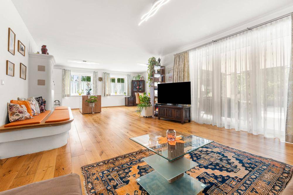 Helles, geräumiges Wohnzimmer mit Holzboden, großzügigen Fenstern und einem traditionellen Kachelofen.