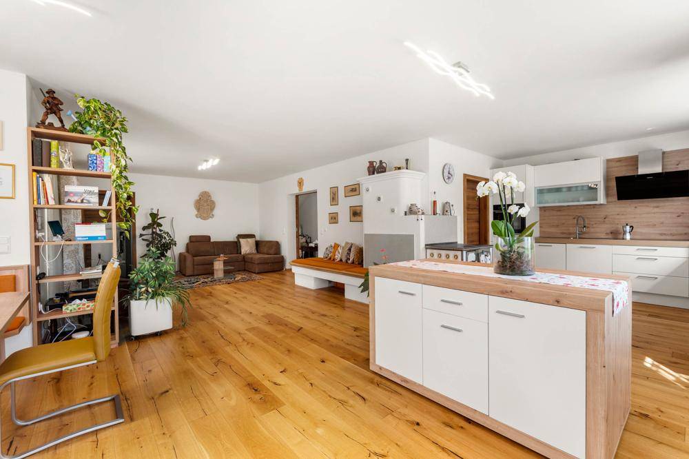 Offener Wohnbereich mit Holzboden, integriertem Arbeitsplatz und Blick auf die moderne Küche.
