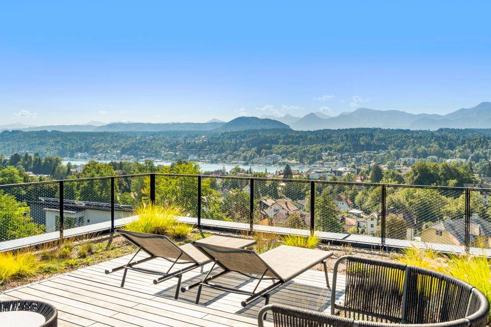 Dachterrasse mit Holzdeck und Liegestühlen, die einen weiten Blick auf See und Berglandschaft bietet.