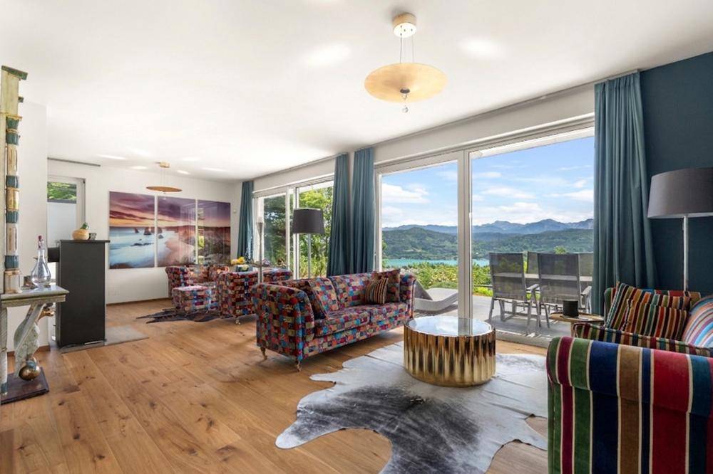 Geräumiges Wohnzimmer mit farbenfrohen Möbeln, Holzboden und großen Fenstern mit Seeblick.