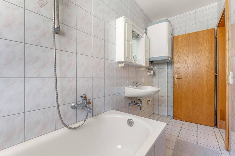 Gefliestes Badezimmer mit Badewanne, integrierter Dusche und Waschbecken.