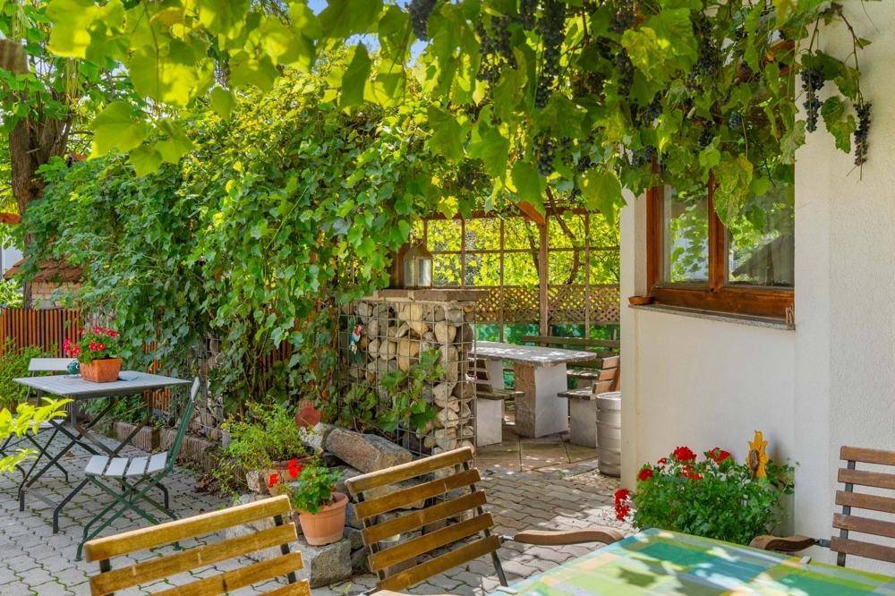 Gemütlicher Gartenbereich mit verschiedenen Sitzgelegenheiten und Gabionenwänden unter schattenspendendem Laub.