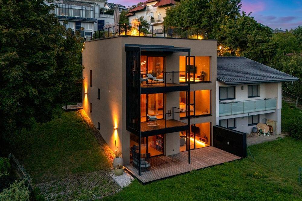 Moderne Architektur des Hauses bei Dämmerung, mit großen Glasflächen und beleuchteten Balkonen.