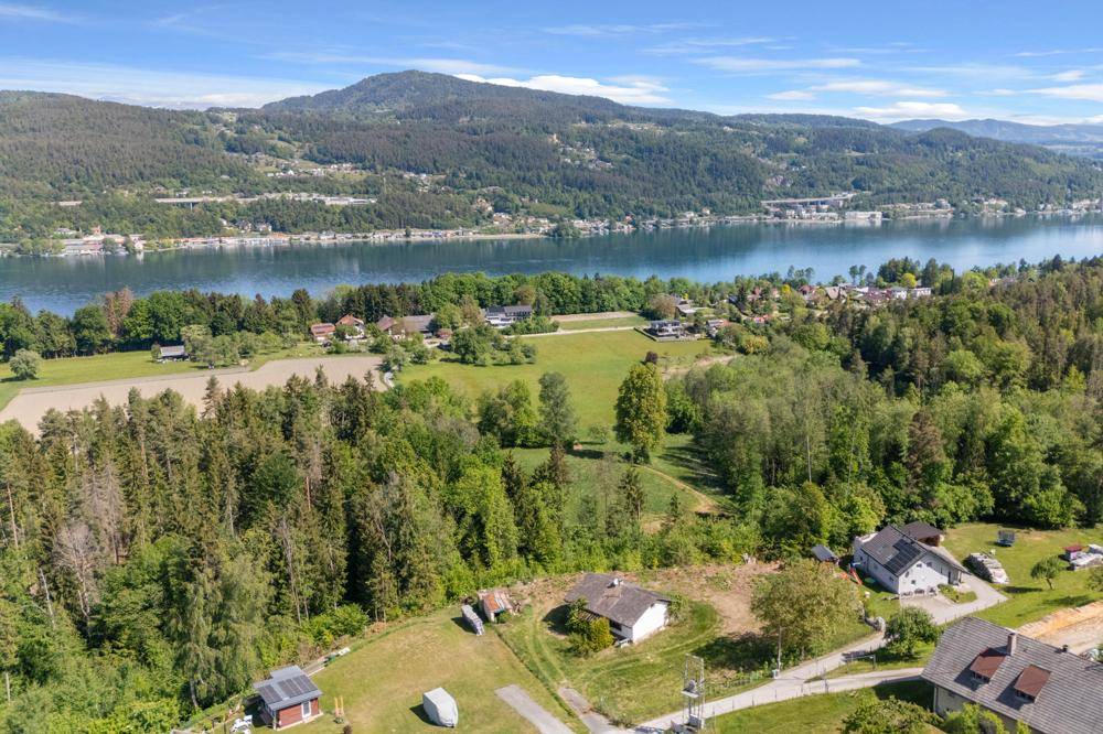 Weitläufige Luftaufnahme der Landschaft mit einem großen See, bewaldeten Hügeln und verstreuten Häusern.