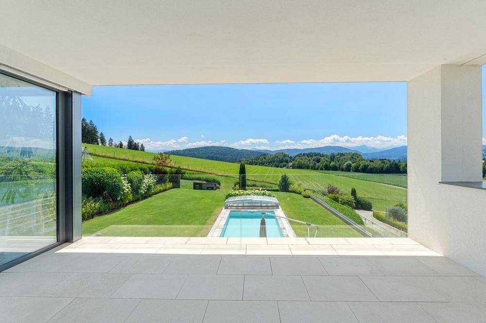 Geräumige überdachte Loggia mit hellem Fliesenboden und weitem Blick auf die grüne Landschaft und Berge.