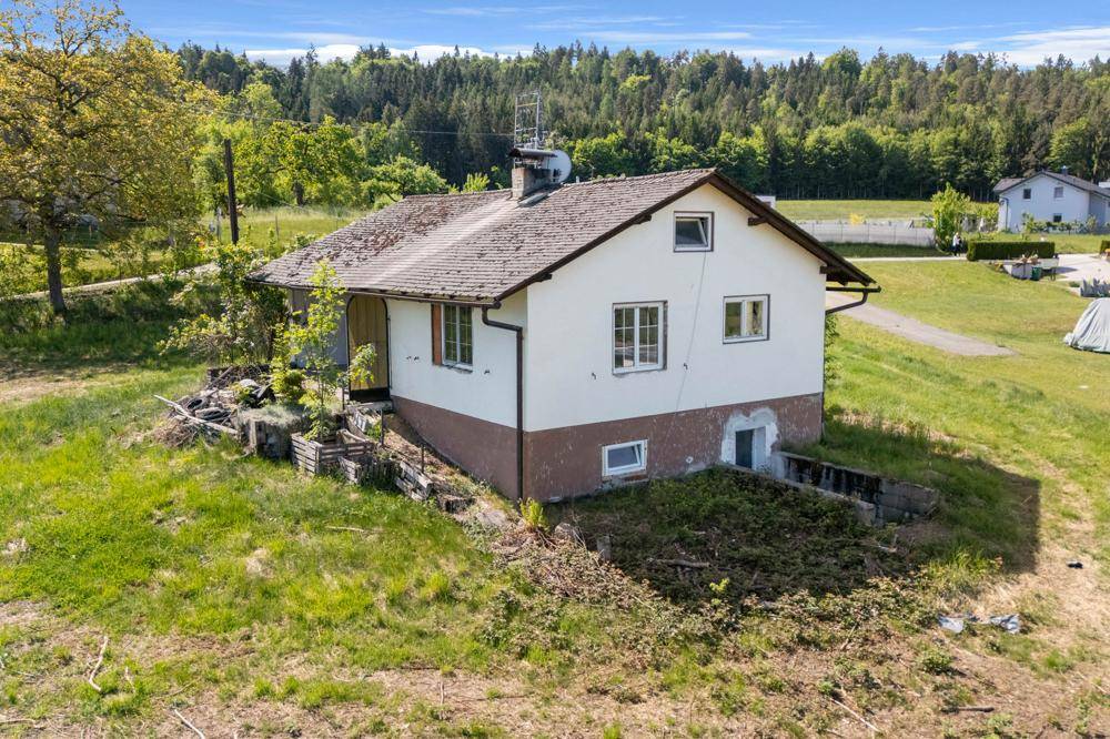 Haus auf einem Hanggrundstück mit sichtbarem Kellerzugang und traditionellem Satteldach.