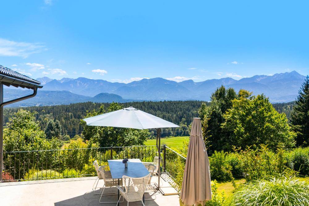 Geräumige Terrasse mit Esstisch, Sonnenschirm und weitem Blick auf die umliegende Berglandschaft.