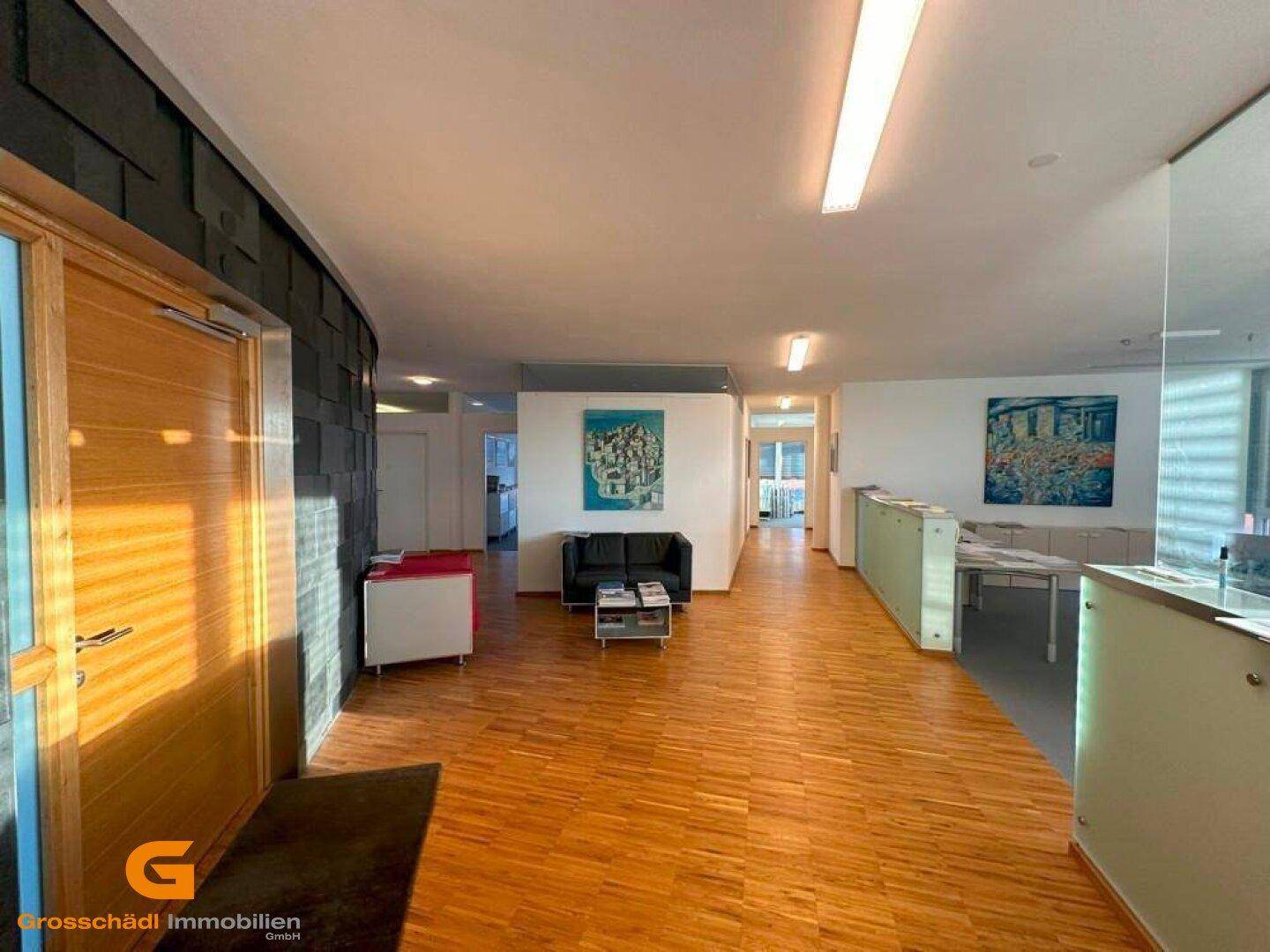 Geräumiger Empfangsbereich im Büro mit Holzparkett, dunkler Wandverkleidung und modernen Möbeln sowie Kunstwerken.