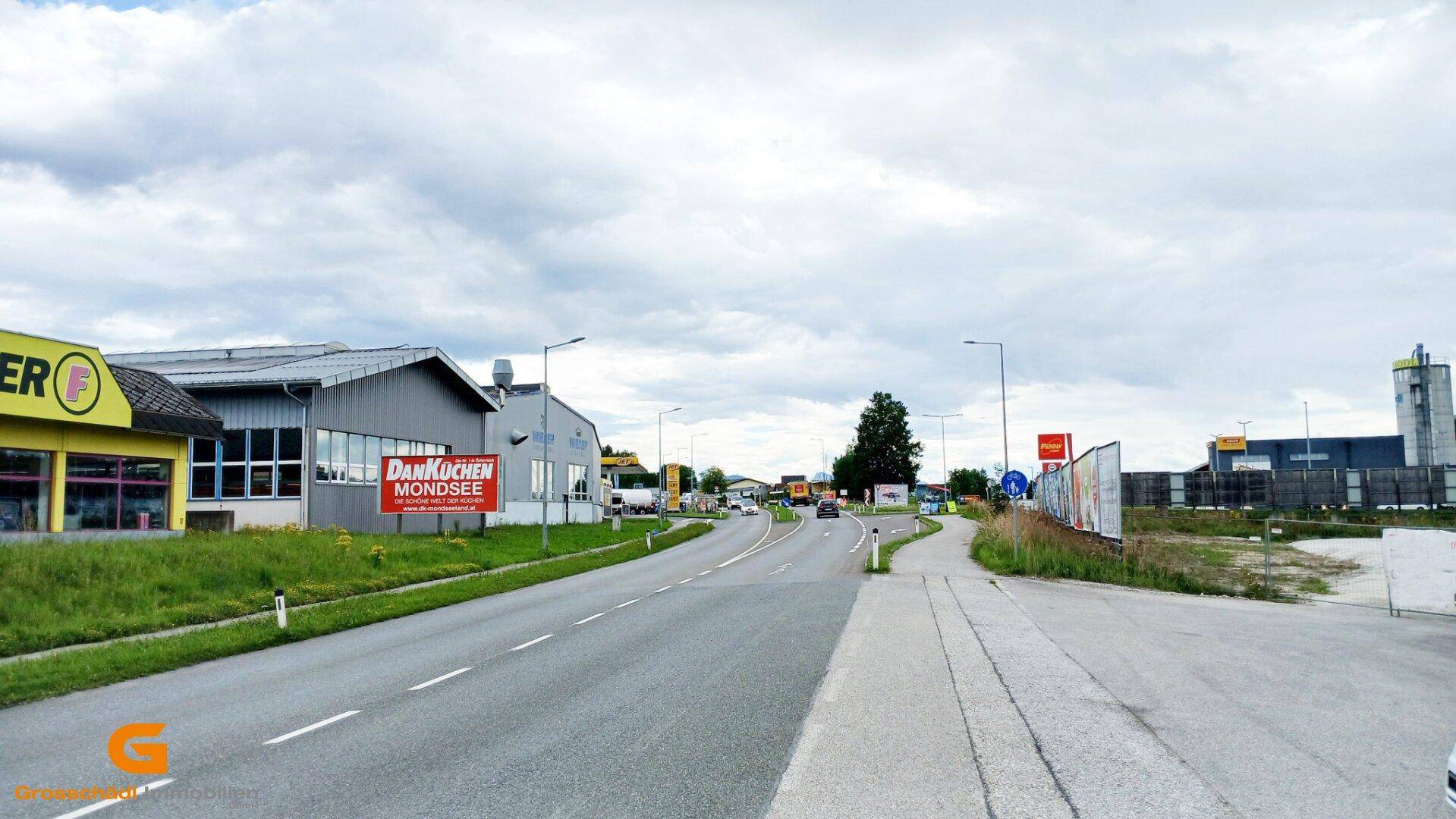 Blick auf eine Landstraße mit Gewerbegebäuden, Werbetafeln und bewölktem Himmel.