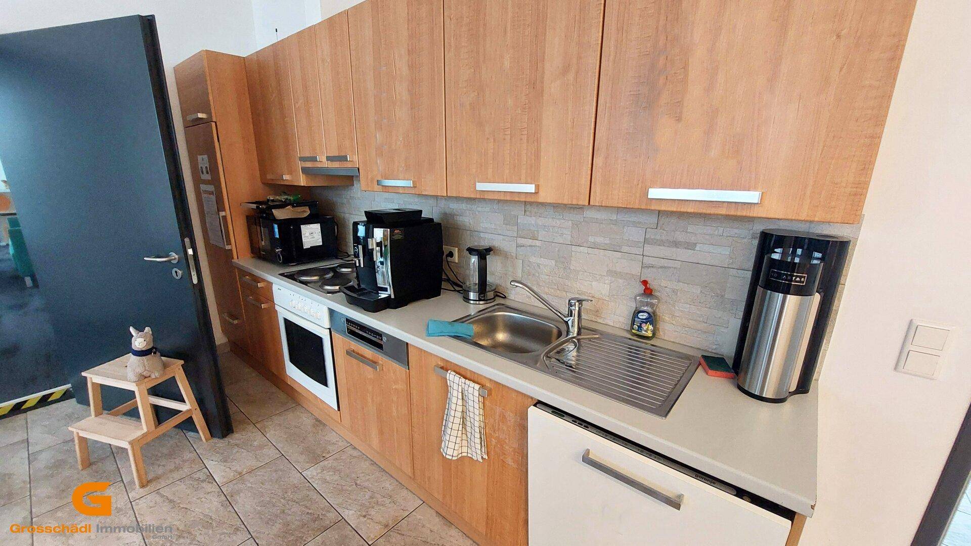 Funktionale Küchenzeile mit Holzschränken, Spüle und verschiedenen Küchengeräten.