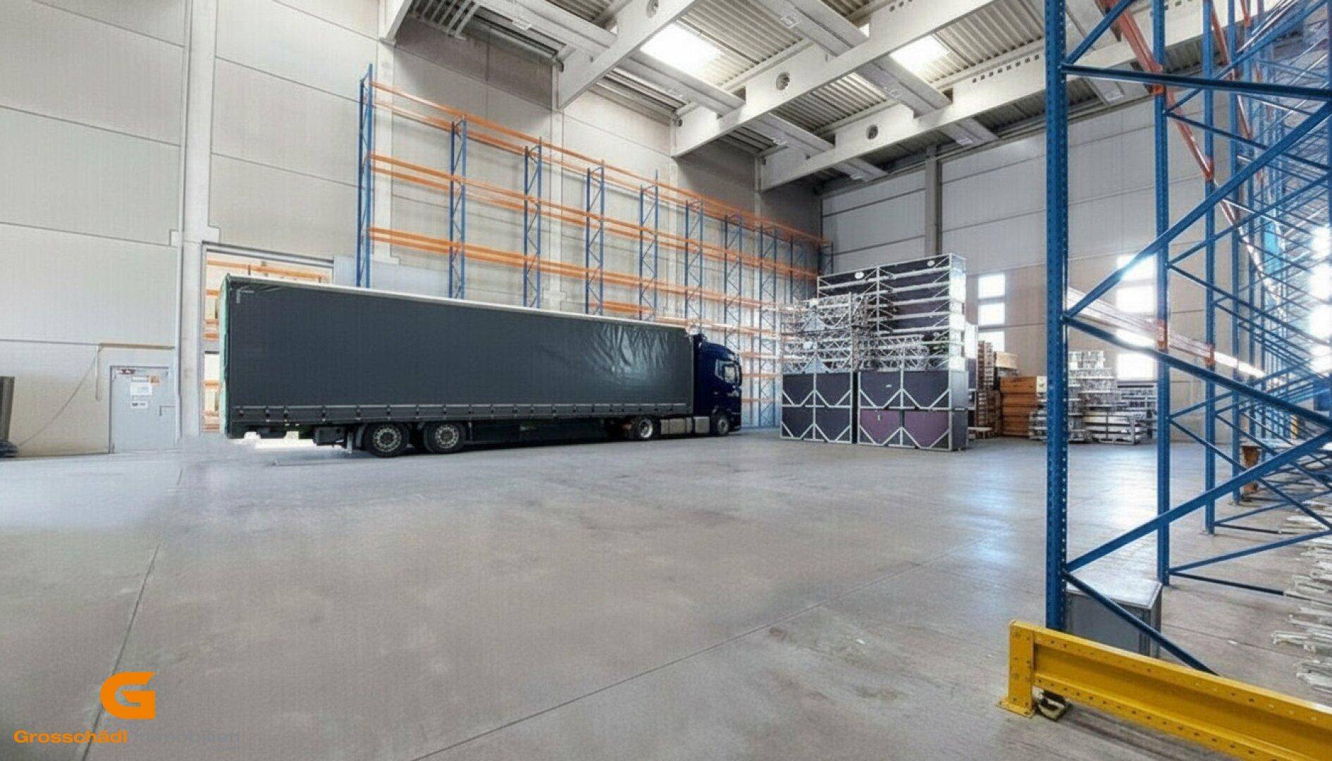 Geräumige Lagerhalle mit hohen Decken, Betonboden, Hochregalen und einem LKW im Inneren, beleuchtet durch Oberlichter.