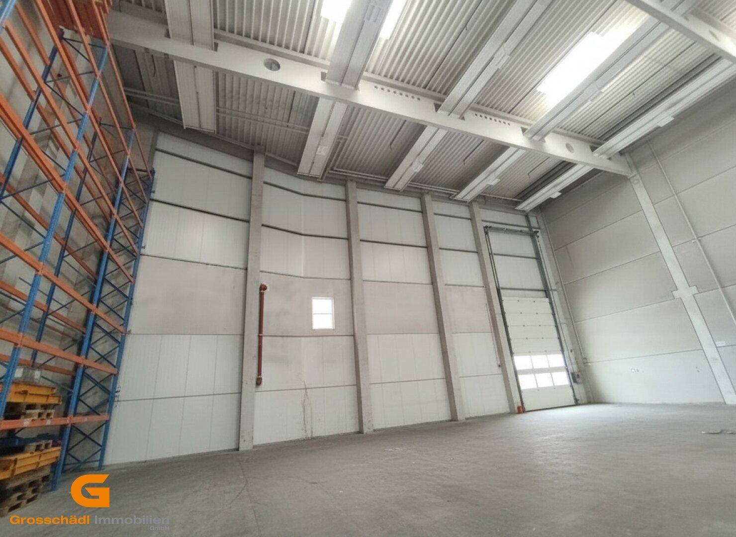 Weitläufige Lagerhalle mit hohen Wänden, Betonboden und einem großen Rolltor für effiziente Anlieferungen.