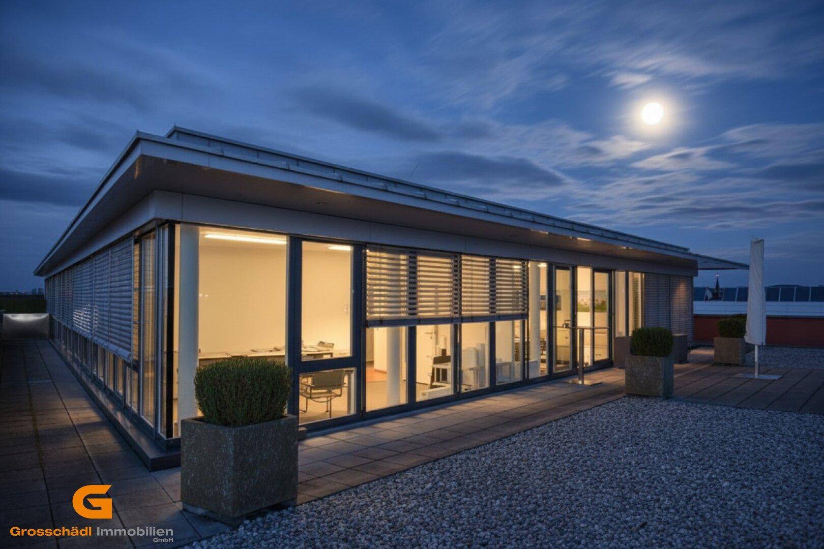 Modernes Gebäude bei Nacht mit beleuchteten Innenräumen und großen Fensterfronten unter Mondschein.