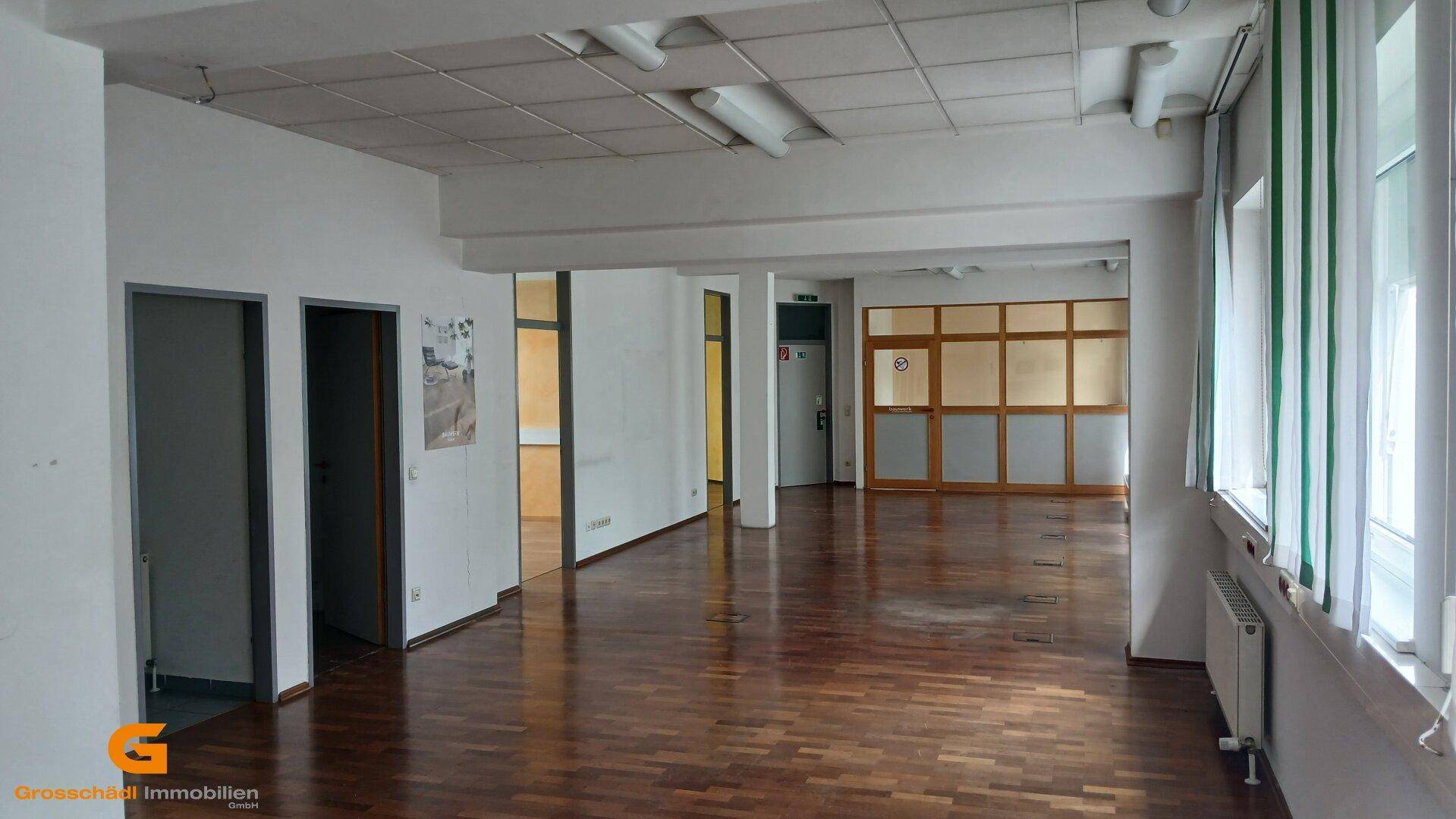 Geräumiger, leerer Büroraum mit Holzboden und großen Fenstern, bereit zur individuellen Gestaltung.