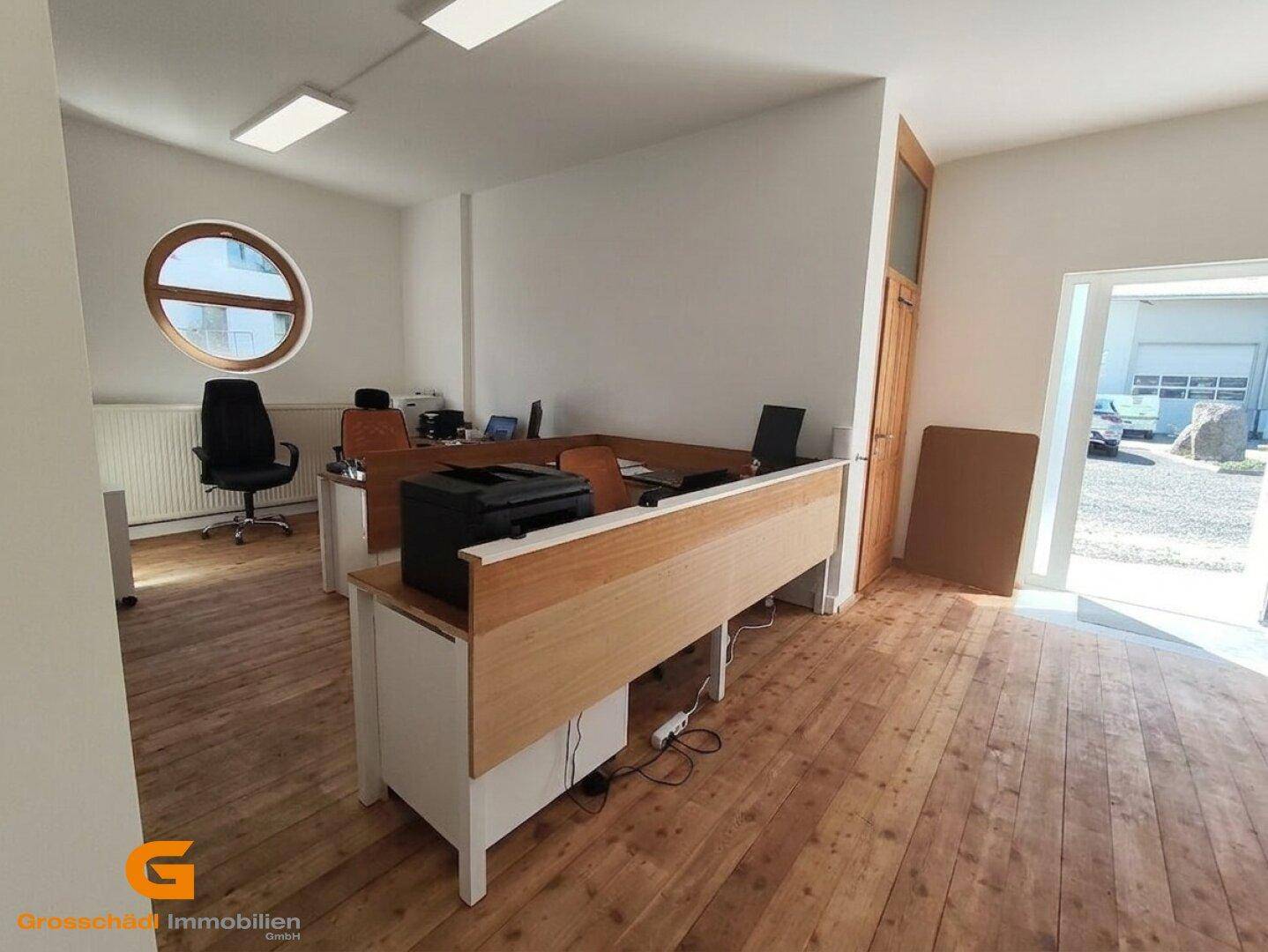 Modernes Büro mit Holzdielenboden, mehreren Schreibtischen und einem markanten runden Fenster.