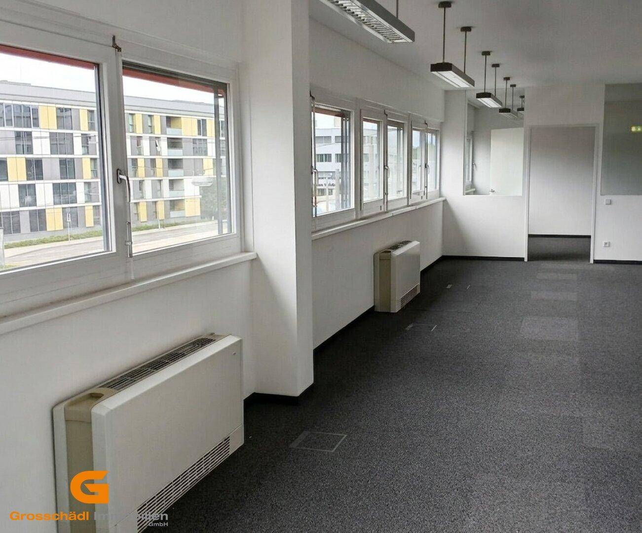 Geräumiger Bürobereich mit vielen Fenstern, Heizkörpern und Blick auf umliegende Gebäude.
