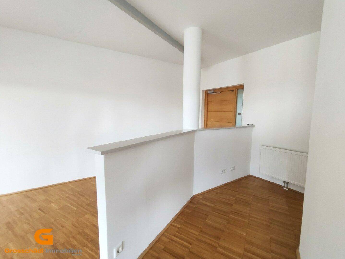 Heller Büroraum mit Holzboden, weiß gestrichenen Wänden und einer halbhohen Trennwand.