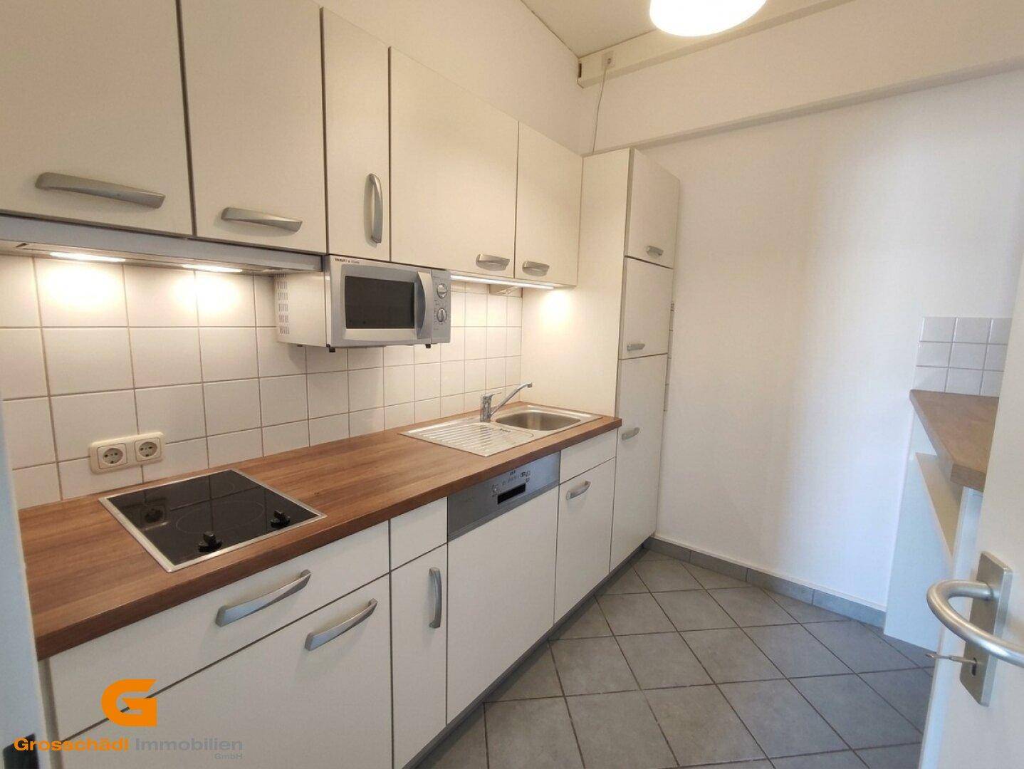 Kleine Küche mit weißen Schränken, Holzarbeitsplatte und integrierten Geräten.