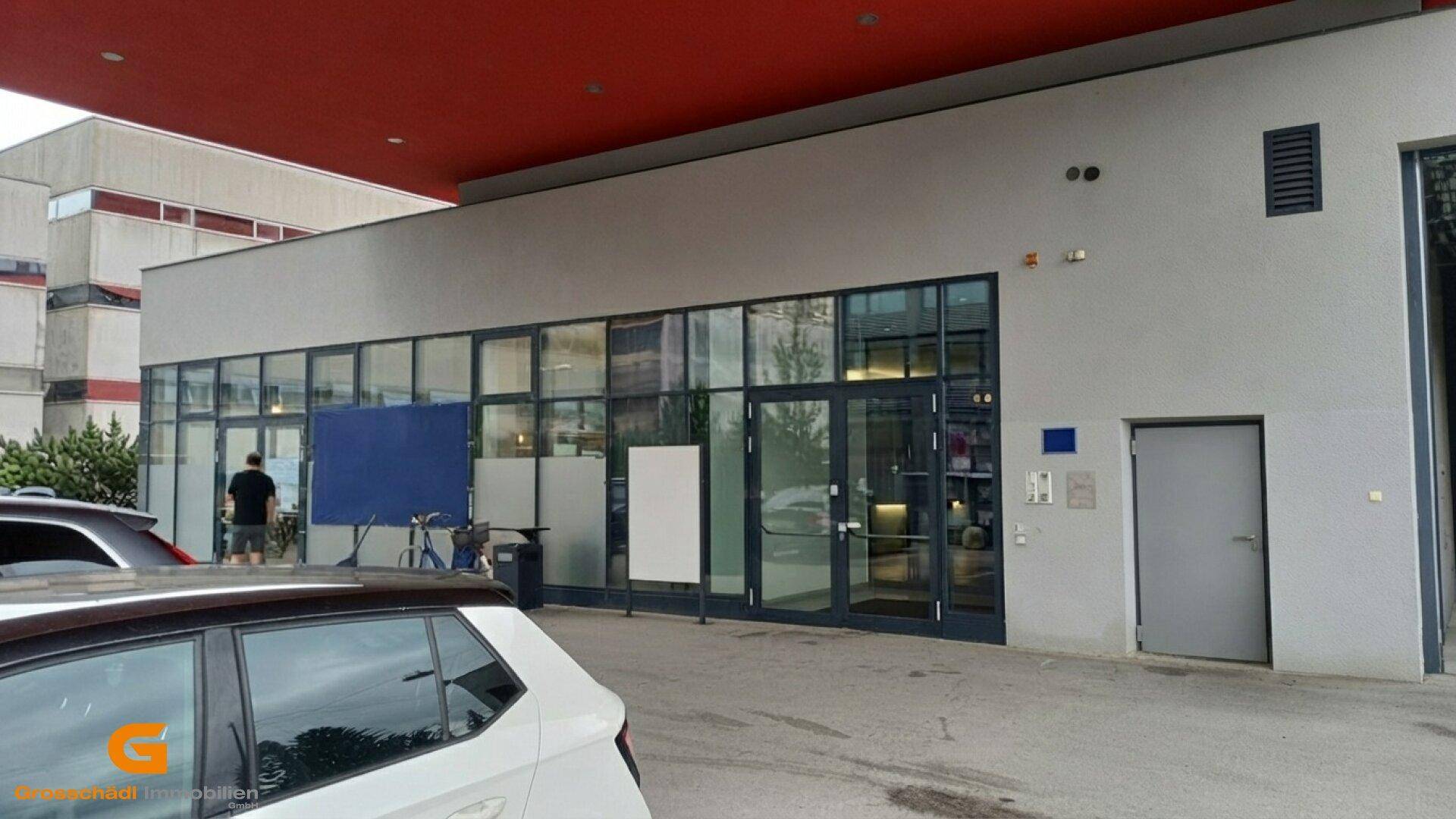 Moderne Gebäudefassade mit großen Glasfenstern und einem roten Vordach, das den Eingangsbereich schützt.