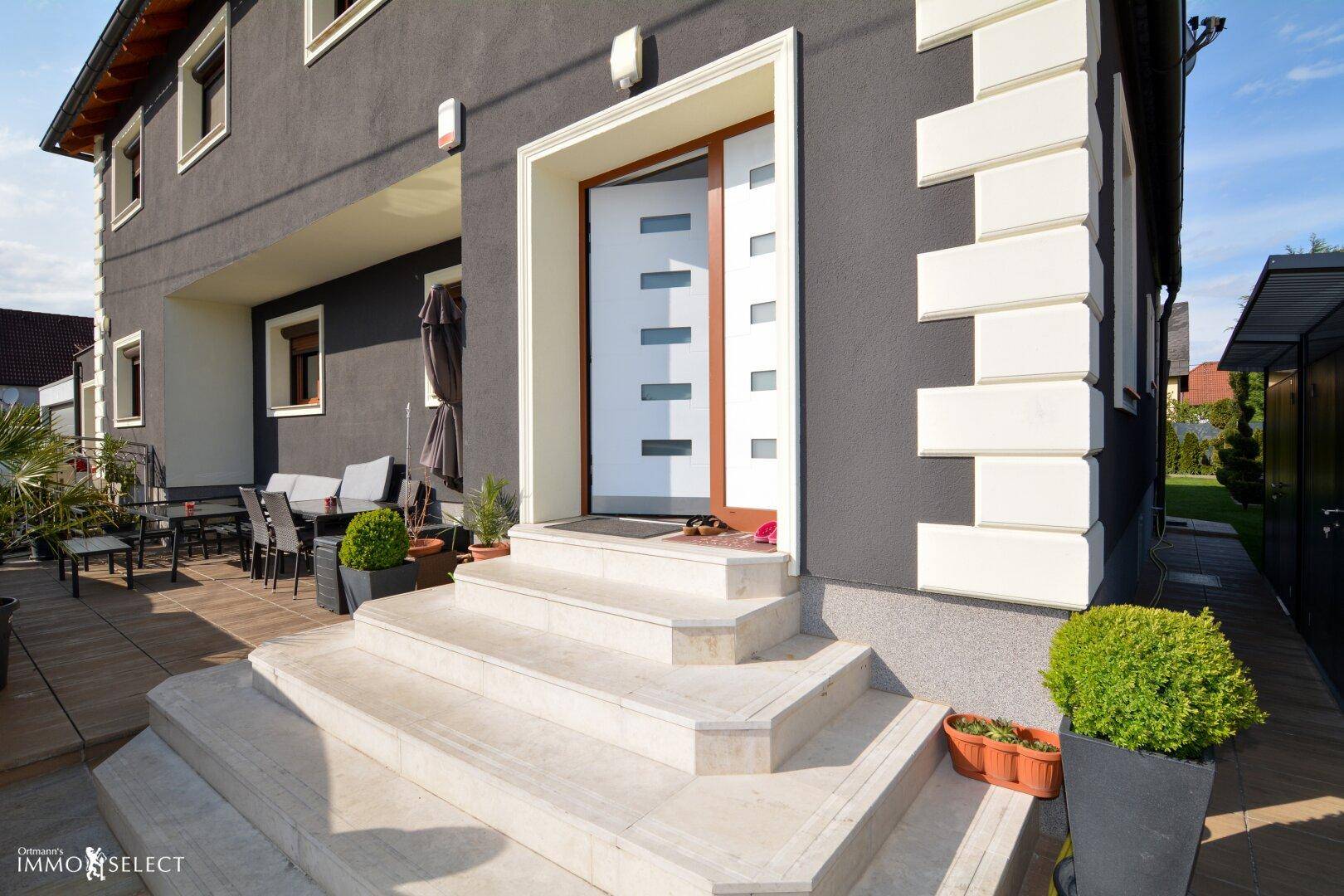 Eingangsbereich des Hauses mit breiter Steintreppe und angrenzender möblierter Terrasse.