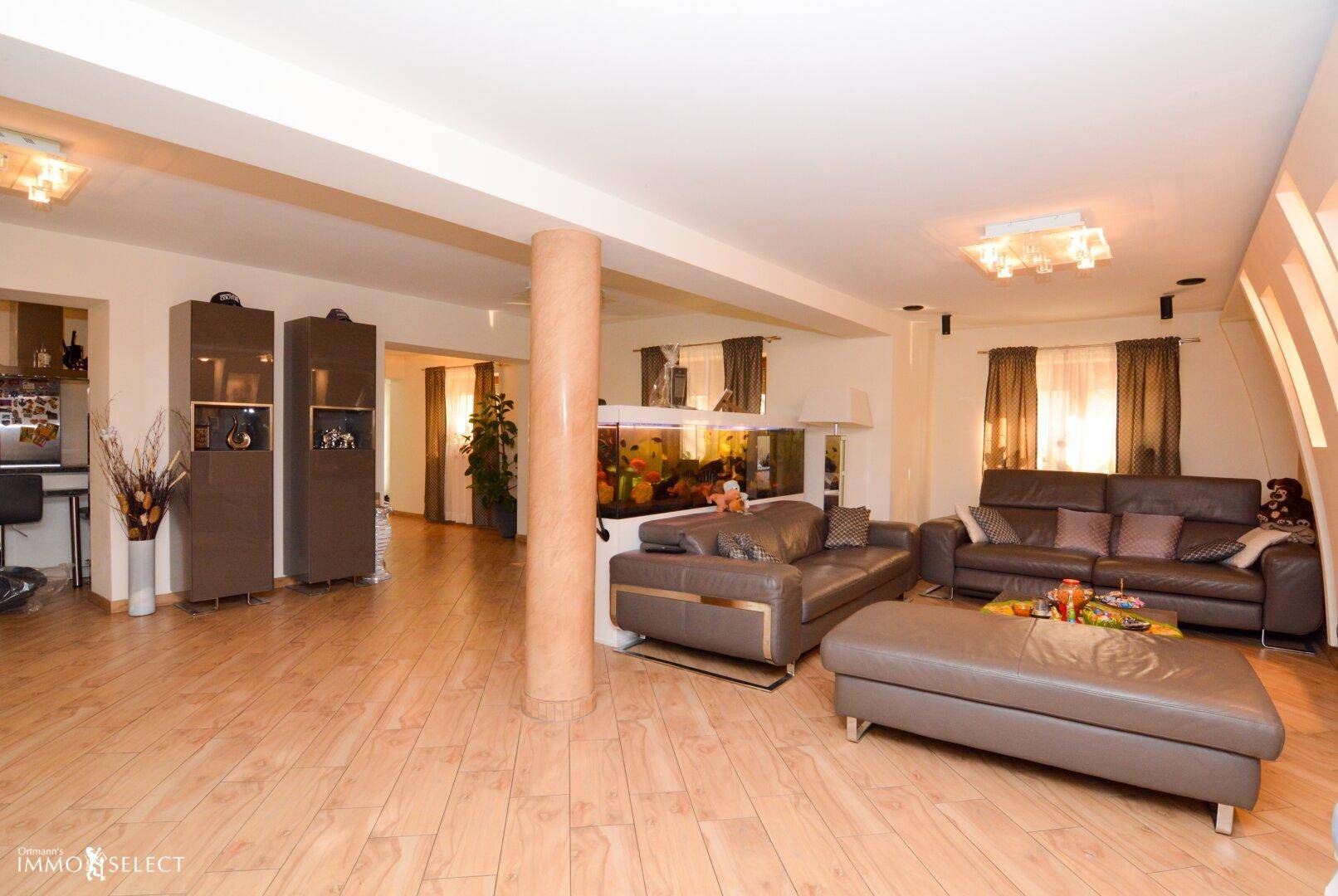 Weitläufiges Wohnzimmer mit Holzboden, Ledersofas und einem dekorativen Aquarium.