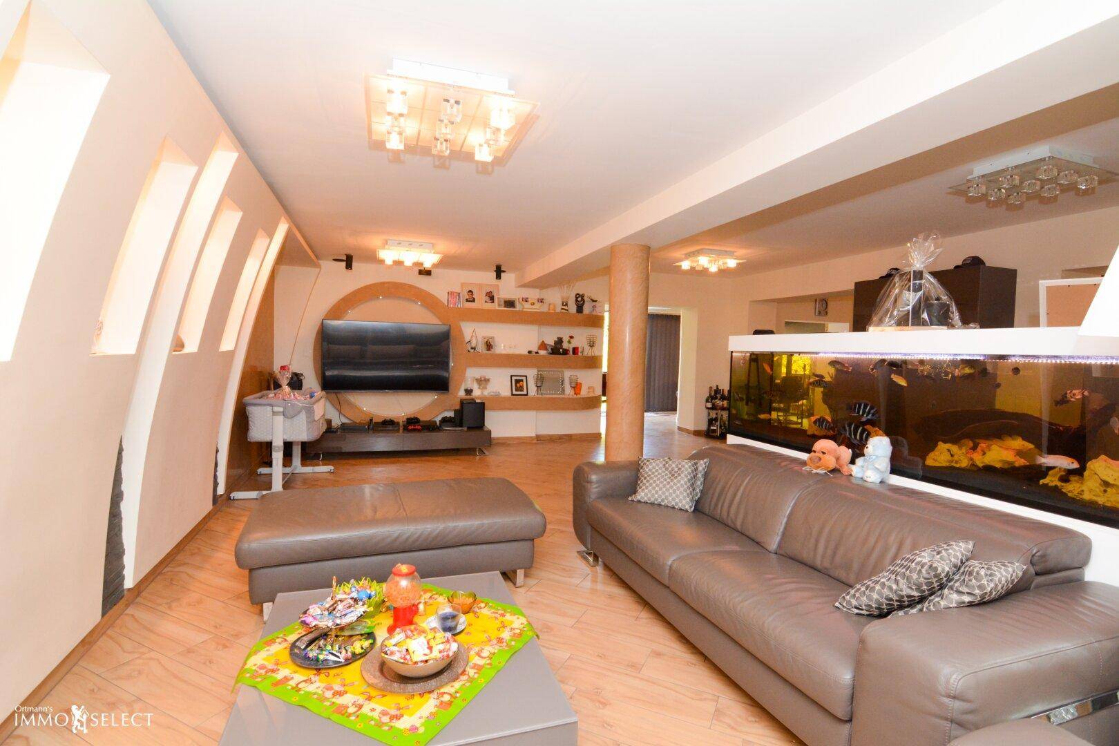 Geräumiges Wohnzimmer mit Holzboden, bequemen Sofas und einem großen Aquarium als Raumteiler.