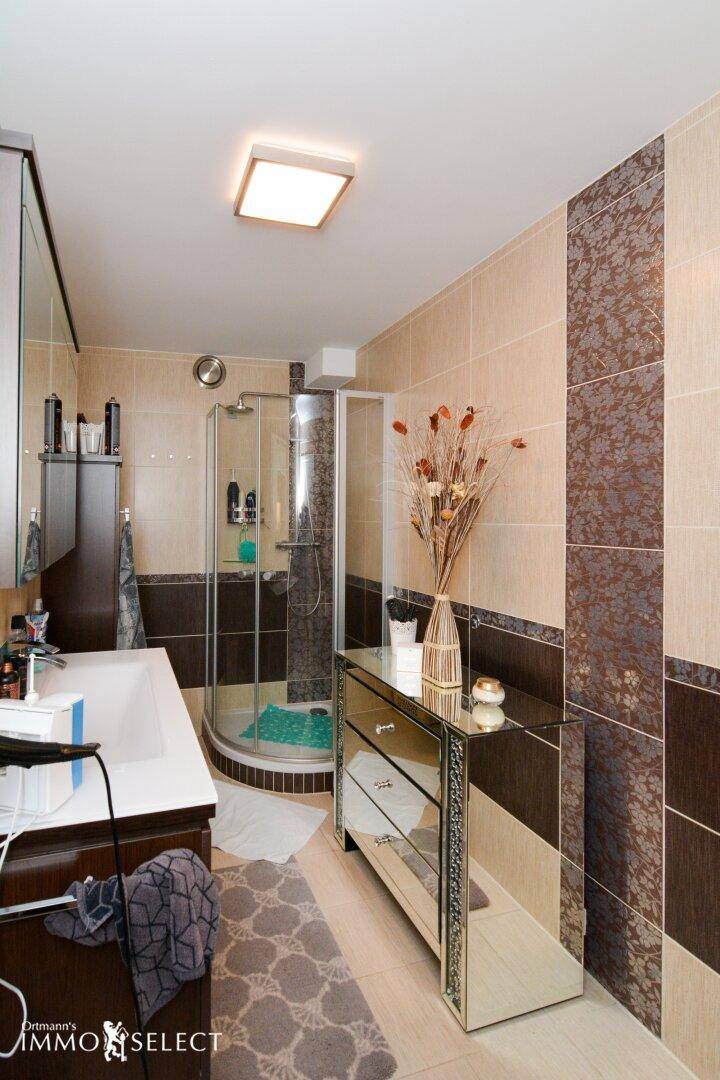 Modernes Badezimmer mit beigefarbenen Fliesen, Duschkabine und Spiegelschrank.